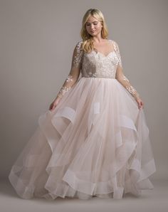 a woman in a dress with long sleeves and sheer tulle skirt, standing on a gray background