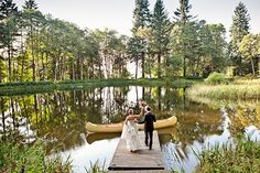 a bride and groom walking on a dock with a canoe