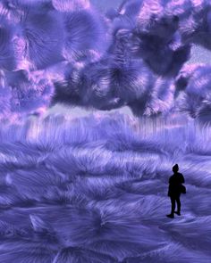 a person standing in the middle of a field with purple grass and clouds behind them