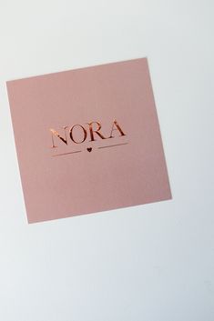 a pink card with the word nora written in gold foil on top of it