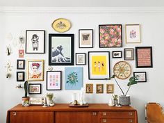 a wall full of framed pictures and other art on it's sideboard in a living room