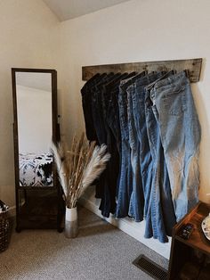 several pairs of jeans are hanging on a rack next to a table with a mirror