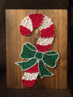 a christmas wreath made out of yarn on a wooden board with a green and red bow