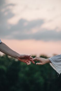 two people reaching out their hands to each other in front of the sun set sky