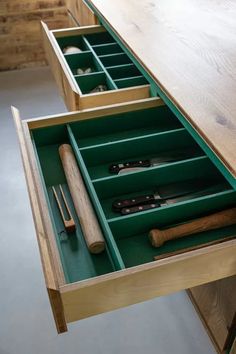 an open drawer with tools in it on top of a wooden table next to other items