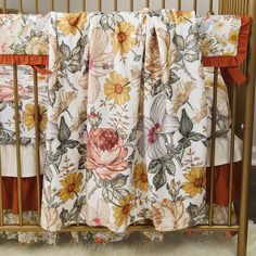 a baby crib with floral bedding and orange ruffles on the bottom