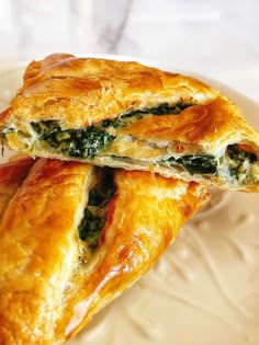 two pastries sitting on top of a white plate covered in cheese and spinach