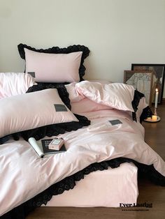 a bed with pink sheets and black ruffles on the bottom, next to a candle