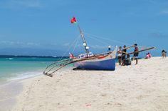 a boat sitting on top of a sandy beach next to the ocean with people standing around it