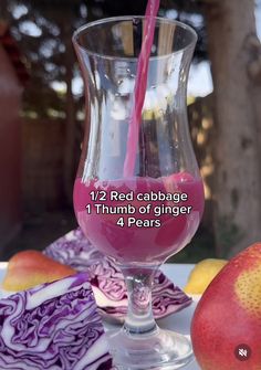 a glass filled with liquid sitting on top of a table next to apples and pears