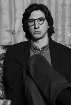 a black and white photo of a man sitting on a couch with his legs crossed