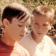 two young boys are looking at something on their cell phone while standing next to each other