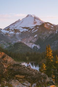 a mountain with snow on it and trees in the foreground, near a lake