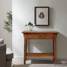 a small wooden table with flowers on it in front of a white wall and chair