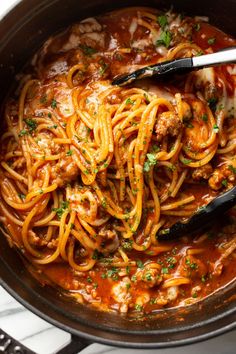 pasta with meat and tomato sauce in a skillet on a marble counter top next to utensils