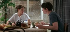 a man and woman sitting at a table with food in front of them on the dining room table