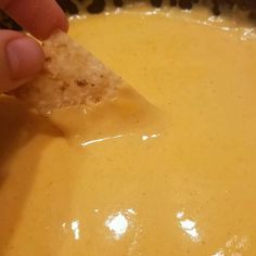 a person dipping cheese into a bowl with a tortilla chip in the middle