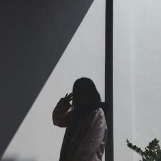 a woman standing next to a tall pole talking on a cell phone while holding a plant in her hand