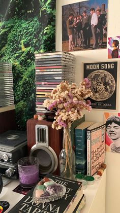 there is a vase with flowers in it on the desk next to books and records