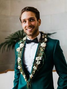 a man wearing a green suit with white flowers in his lapel and black bow tie