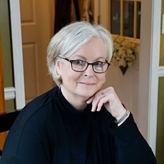 a woman wearing glasses sitting in front of a door with her hand on her chin