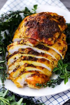 a white plate topped with sliced chicken covered in sauce and garnished with parsley