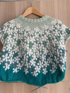 a green sweater with white flowers is hanging on a wooden hanger next to yarn