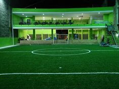 an empty soccer field at night in front of a large building with lights on it