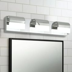 a bathroom mirror with three lights above it and a white tiled wall behind it,