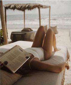 a woman laying on the beach reading a book