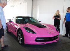 two people are standing next to a pink sports car