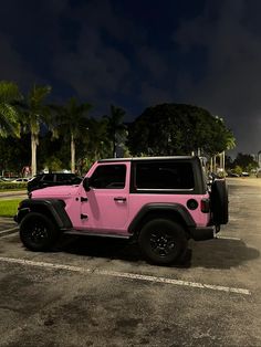 a pink jeep is parked in a parking lot at night with palm trees behind it