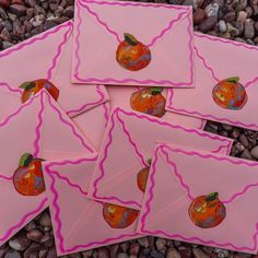 four pink envelopes with pictures of oranges on them sitting on some rocks and pebbles