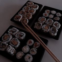 two trays filled with sushi and chopsticks on top of a table