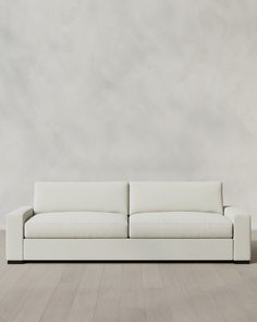 a white couch sitting on top of a hard wood floor next to a gray wall