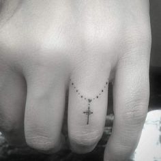 a small cross tattoo on the middle finger is shown in black and white ink,