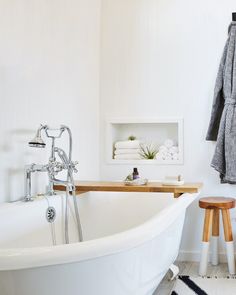 a white bath tub sitting in a bathroom next to a wooden stool and towel rack