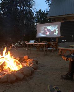 people sitting around a campfire with a projector screen on the wall behind them