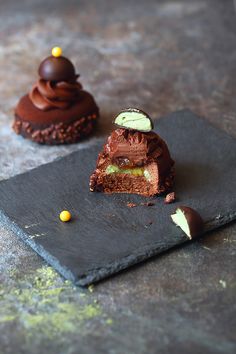 two pieces of chocolate dessert sitting on top of a slate plate