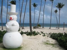 a snowman with a broom and top hat on the beach next to palm trees