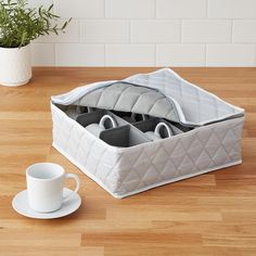 a white coffee cup and saucer on a wooden table next to an open storage container