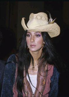 a woman wearing a cowboy hat with feathers on it's brim and purple eyeshade