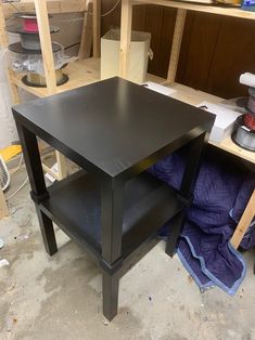 a black table sitting on top of a wooden floor next to a pile of wood