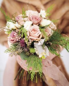 a bouquet of flowers sitting on top of a glass vase filled with greenery and pink roses