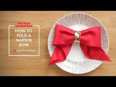 a white plate topped with a red bow on top of a wooden table next to a knife and fork