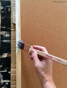 a person holding a paint brush in front of a piece of cardboard that has been painted