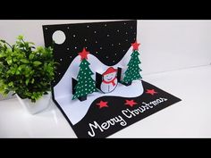 a christmas card with a snowman and trees on it, next to a potted plant