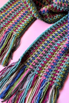 a multicolored knitted scarf with fringes on pink background, close up