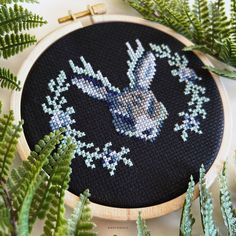 a cross - stitch pattern on a black background with green plants and fern leaves around it