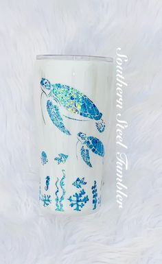 a blue and white tumbler with a turtle on it's side sitting on a fluffy surface